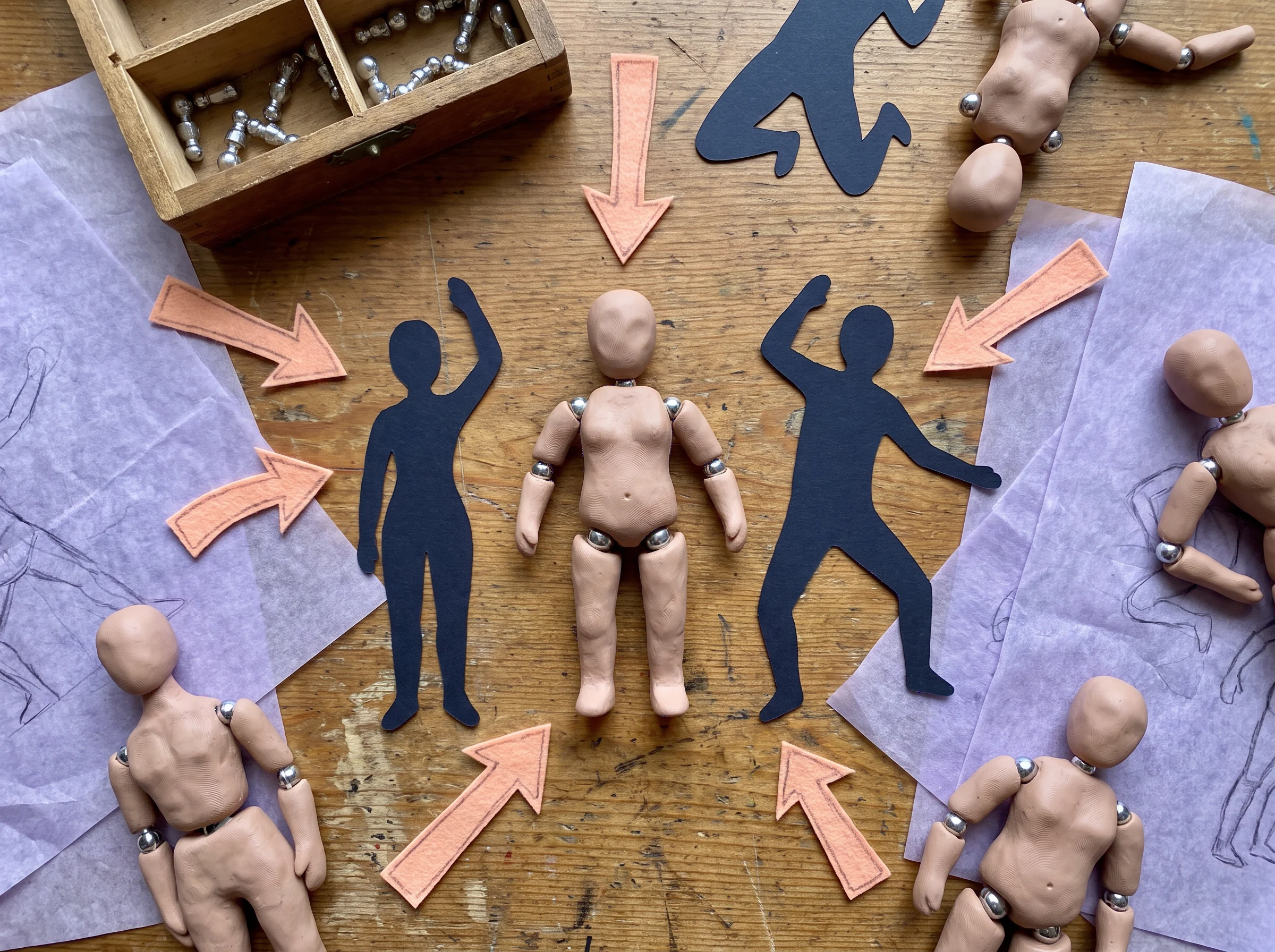 Top view of small maquettes, blue silhouette cutouts, arrows, and pose references